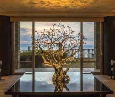 Lobby with sculptural tree centerpiece reflected on table, floor-to-ceiling windows and distant sea view at KAMENOI HOTEL Atami