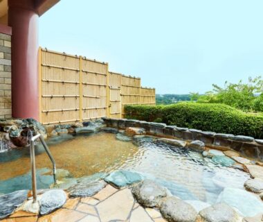 Stone outdoor onsen bath with bamboo fence and green hills at KAMENOI HOTEL Ichinoseki Iwate