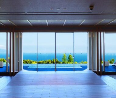 Lobby with floor-to-ceiling windows framing outdoor pool and sea at KAMENOI HOTEL Izukogen, Shizuoka