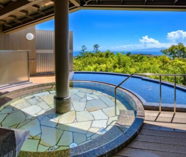 Round tiled onsen bath on wooden deck overlooking treeline and distant sea at KAMENOI HOTEL Izukogen Shizuoka