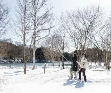 Two people walking in a snowy park with bare trees near KAMENOI HOTEL Okunikko in Tochigi Japan