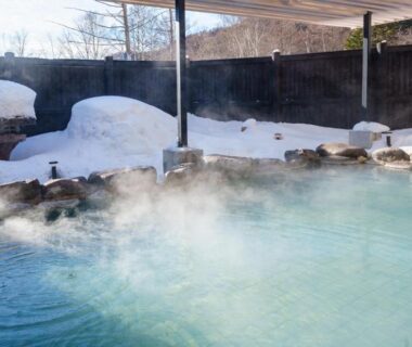 Steaming outdoor onsen bath with snow-covered rocks and partial shelter at KAMENOI HOTEL Okunikko Tochigi