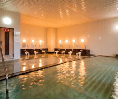 Communal indoor onsen bath with tiled pool, washing stations and stools at KKR Numazu Hamayu in Shizuoka