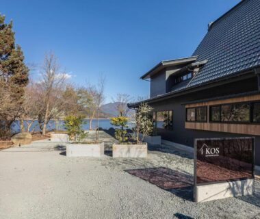Gravel entrance and sign for KOS Restaurant & Hotel by a lakeside with traditional Japanese building