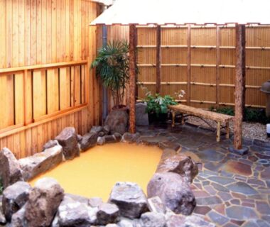 Outdoor stone onsen with bamboo fence and wooden bench at Kadonobo Ryokan in Hyōgo