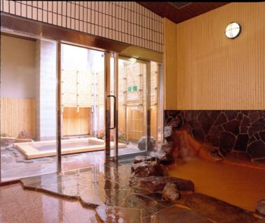 Stone soaking bath with wooden walls and glass doors leading to outdoor bathing area at Kadonobo Ryokan Hyōgo