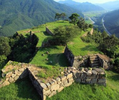 Stone castle ruins on grassy hilltop with forested mountains and a distant river in Hyōgo
