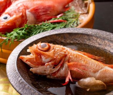 Simmered whole fish on ceramic plate with garnish and wooden serving tub behind, traditional ryokan meal at Kagariya, Hokkaidō