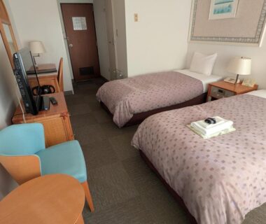 Twin beds with desk, TV, lamp and folded towels in Kagetsuen room, Kanagawa