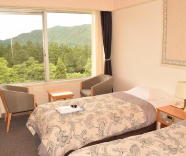 Twin beds with patterned covers, seating area by large window overlooking green hills at Kagetsuen ryokan in Kanagawa