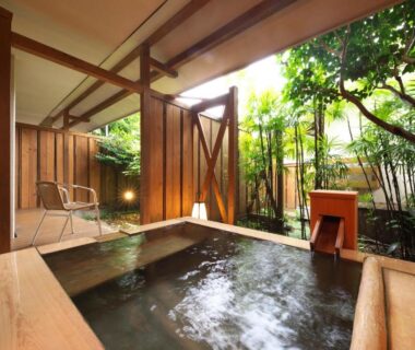 Wooden onsen bath opening to a secluded garden with wooden fence and chairs at Kagetsutei, Shizuoka