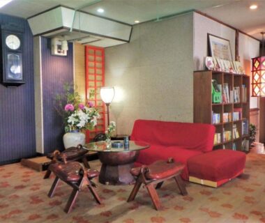 Lobby seating area with red sofa, low wooden table, stools, shoji screen and decorative clock at Kaigetsu, Mie