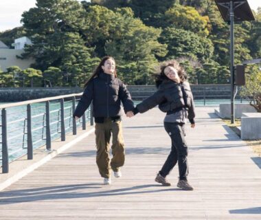 Two people holding hands walking on a waterfront boardwalk near Kaigetsu in Mie, Kansai, Japan