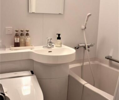 Small unit bathroom featuring a bidet toilet, sink, mirror, handheld shower and compact soaking tub at Kaigetsu in Mie
