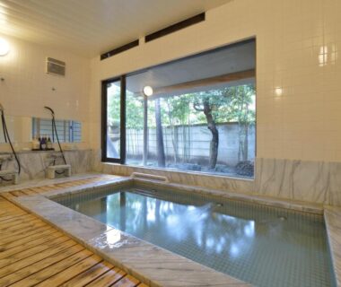 Tiled indoor bath with shower stations and wooden edge, large window overlooking courtyard at Kaihinsou Kamakura Kanagawa
