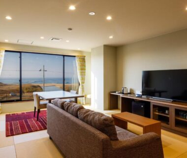 Tatami room with sofa, low table, TV and balcony window overlooking distant landscape at Kaikatei Hanagozen, Kyoto