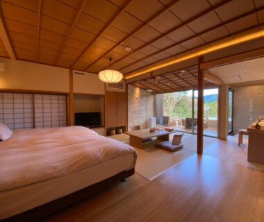 Western bed room with shoji screens, low seating, sliding glass doors to wooden terrace and garden view