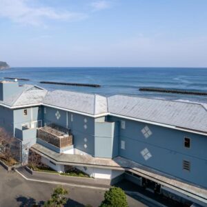 Blue coastal ryokan building Kaiyutei along Shizuoka coastline with road and parking area