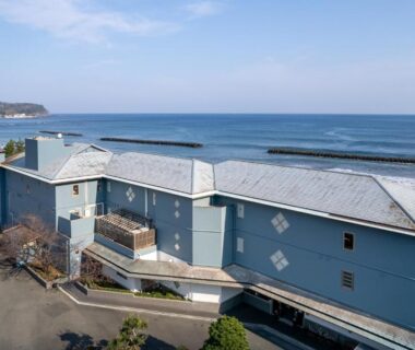 Blue coastal ryokan building Kaiyutei along Shizuoka coastline with road and parking area