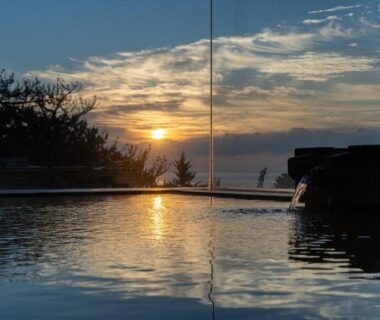 Outdoor onsen bath reflecting sunset at Kaiyutei Shizuoka with silhouetted trees and distant water horizon