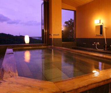 Indoor wooden onsen bath with warm lighting and open window overlooking distant hills at Kakimotoya Nara