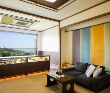 Bright tatami room with low table, sofa seating and large window overlooking greenery at Kakimotoya Nara
