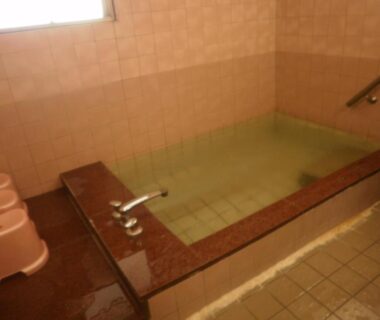 Tiled indoor bathing area with stools, faucet and handrail at Kakiya Ryokan in Kanagawa