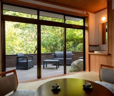 Traditional tatami room opening to a wooden terrace with outdoor seating and lush garden at Kakureisen, Saga
