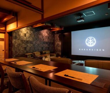 Dining room with long wooden table, placemats, chairs and projector screen at Kakureisen Saga