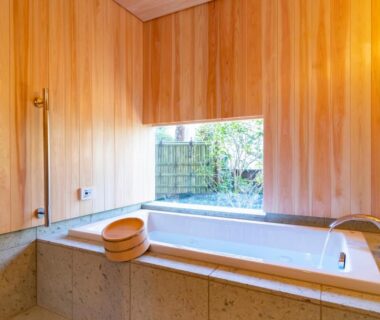 Wood-paneled bathroom with stone soaking tub, wooden wash bucket and low garden window at Kamakura COCON, Kanagawa
