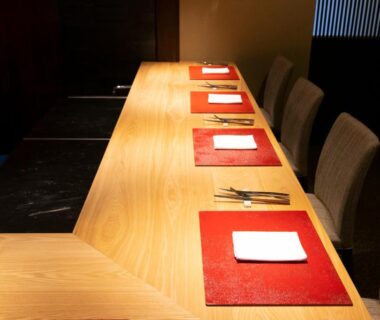 Long wooden counter with red placemats, chopsticks and seating at Kamakura COCON in Kanagawa, Japan
