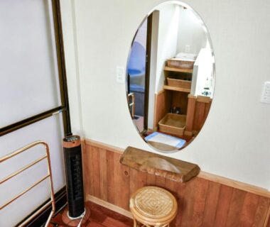 Wooden dressing area with oval mirror, small stool and towel rack at Kamegawa Onsen HATAGO Yuyu in Ōita