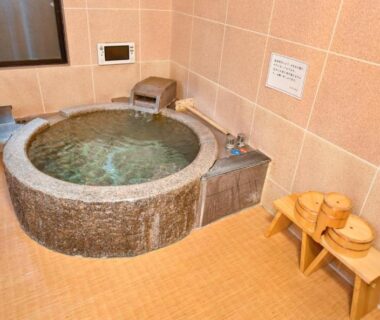 Round stone onsen tub in tiled indoor bathing room with wooden stools and bathing buckets