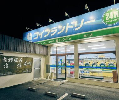 Night lit 24-hour coin laundry storefront with signage near Kamegawa Onsen HATAGO Yuyu, Ōita