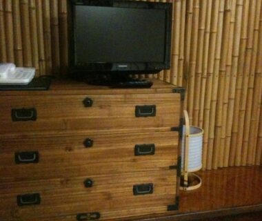 Tansu chest topped by a small TV and telephone with bamboo wall paneling in a Nagano ryokan room