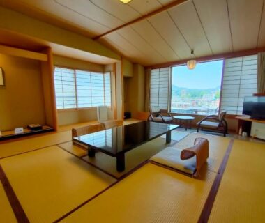 Traditional tatami room with low table, zabuton seating and shoji screens, large windows overlooking town and distant hills