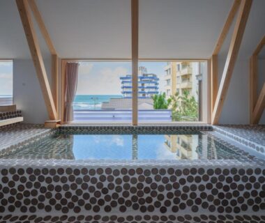 Tiled indoor onsen bath with large window overlooking city and distant water at Kameya Hotel Yamagata