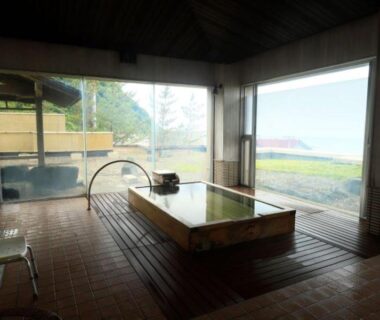 Wooden indoor onsen bath inside large windowed room overlooking coastline at Kameya Hotel Yamagata