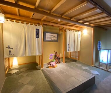 Noren curtains at ryokan entrance with stone step, lanterns and floral display, Kameya Rakan, Shizuoka