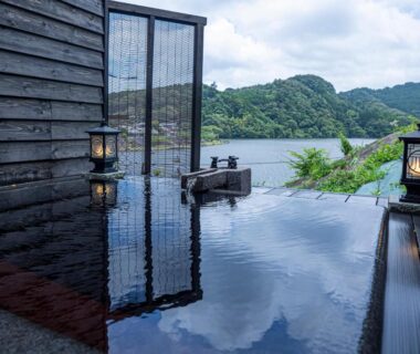 Outdoor onsen terrace with lanterns overlooking lake and wooded hills at Kameyama Onsen Hotel, Chiba