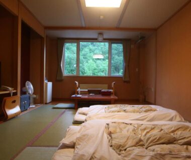 Traditional tatami room with futons and low table, window framing green trees at Kamihoroso, Hokkaidō