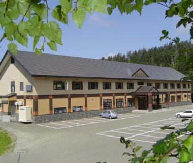 Two-story ryokan exterior with parking and leafy foreground at Kamihoroso, Hokkaidō