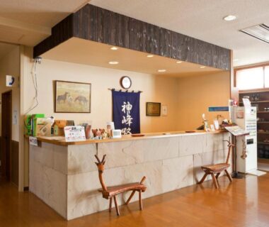 Stone reception desk with traditional banner, wooden branch chairs and hallway at Kamihoroso ryokan, Hokkaidō