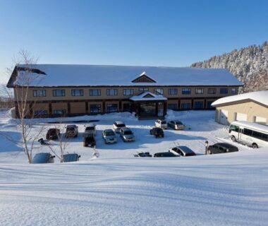 Kamihoroso exterior amid snowy grounds, parking area and forested hills in Hokkaidō