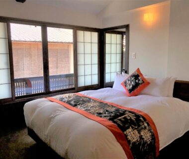 Low Western-style bed with decorative runner, shoji screens and wooden balcony at Kamishichiken Oku Kyoto