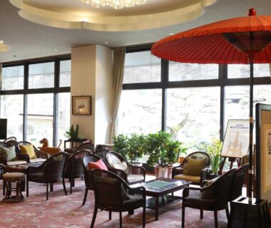 Interior lounge with seating, red parasol and large windows at Kamiyamada Hotel in Nagano Chūbu