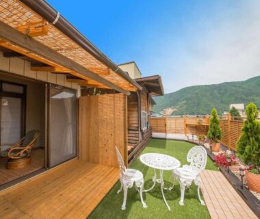 Wooden deck terrace with white metal table and chairs, sliding doors and mountain view at Kamiyamada Hotel Nagano