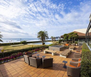 Outdoor tiled terrace with wicker lounge seating facing beach and palm trees at Kamogawa Grand Hotel Chiba