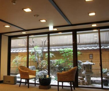 Two wicker chairs facing a courtyard garden with stone lantern behind glass at Kamogawakan Kyoto