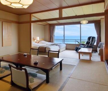 Spacious tatami room with low table, futon, shoji screens and wide window overlooking water at Kamogawakan, Chiba